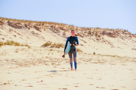 Une adolescente marchant sur la plage du Cap Ferret pour sa leçon de surf